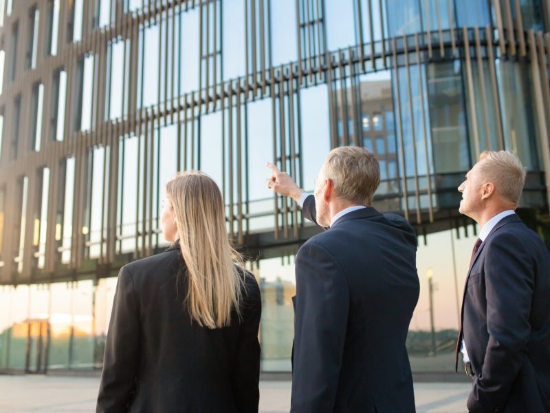 group-business-partners-formal-suits-pointing-office-building-meeting-outdoors-discussing-real-property-back-view-commercial-real-estate-concept_74855-7313